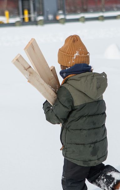 Un enfant porte des morceaux de bois alors qu'il marche dans la neige.
