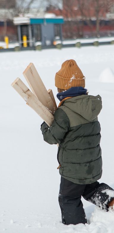 A child walking in the snow and holding pieces of wood.